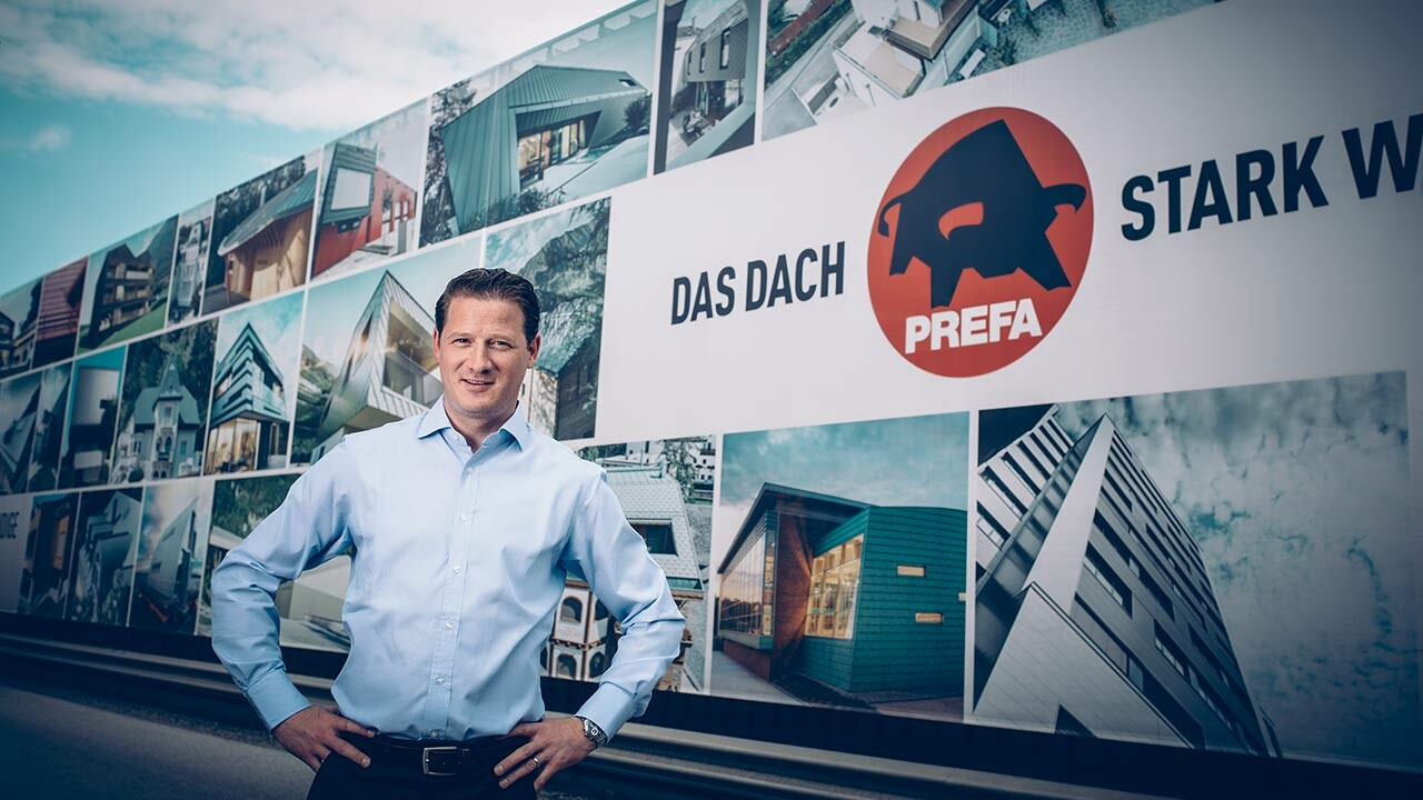PREFA Geschäftsführer, Leopold Pasquli, vor dem Firmengebäude mit PREFA Logo.