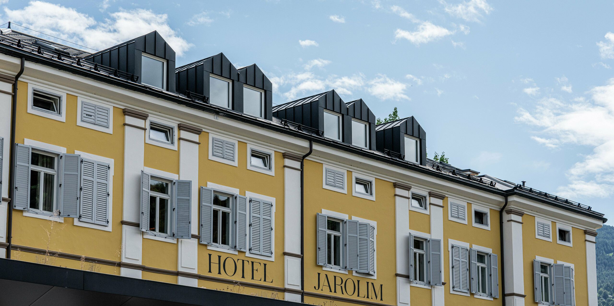 Detailansicht des Hotels Jarolim in Brixen mit modernen Dachgauben, verkleidet mit PREFA Aluminium. Die präzise gefertigten Gauben und die Dachplatten R.16 in P.10 Schwarz unterstreichen die Eleganz und Funktionalität des Daches. Das langlebige und witterungsbeständige PREFA Dach fügt sich nahtlos in die historische Architektur ein und verbindet Tradition mit Innovation. Die perfekte Wahl für langlebige, ästhetische und hochwertige Dachlösungen.