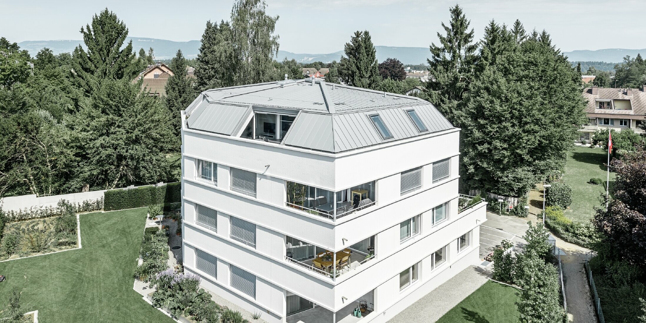 Schlichtes Mehrfamilienhaus mit PREFA Prefalz in Patina Grau; Die Fassade ist weiß verputzt mit großzügigen Loggien an der Außenecke.