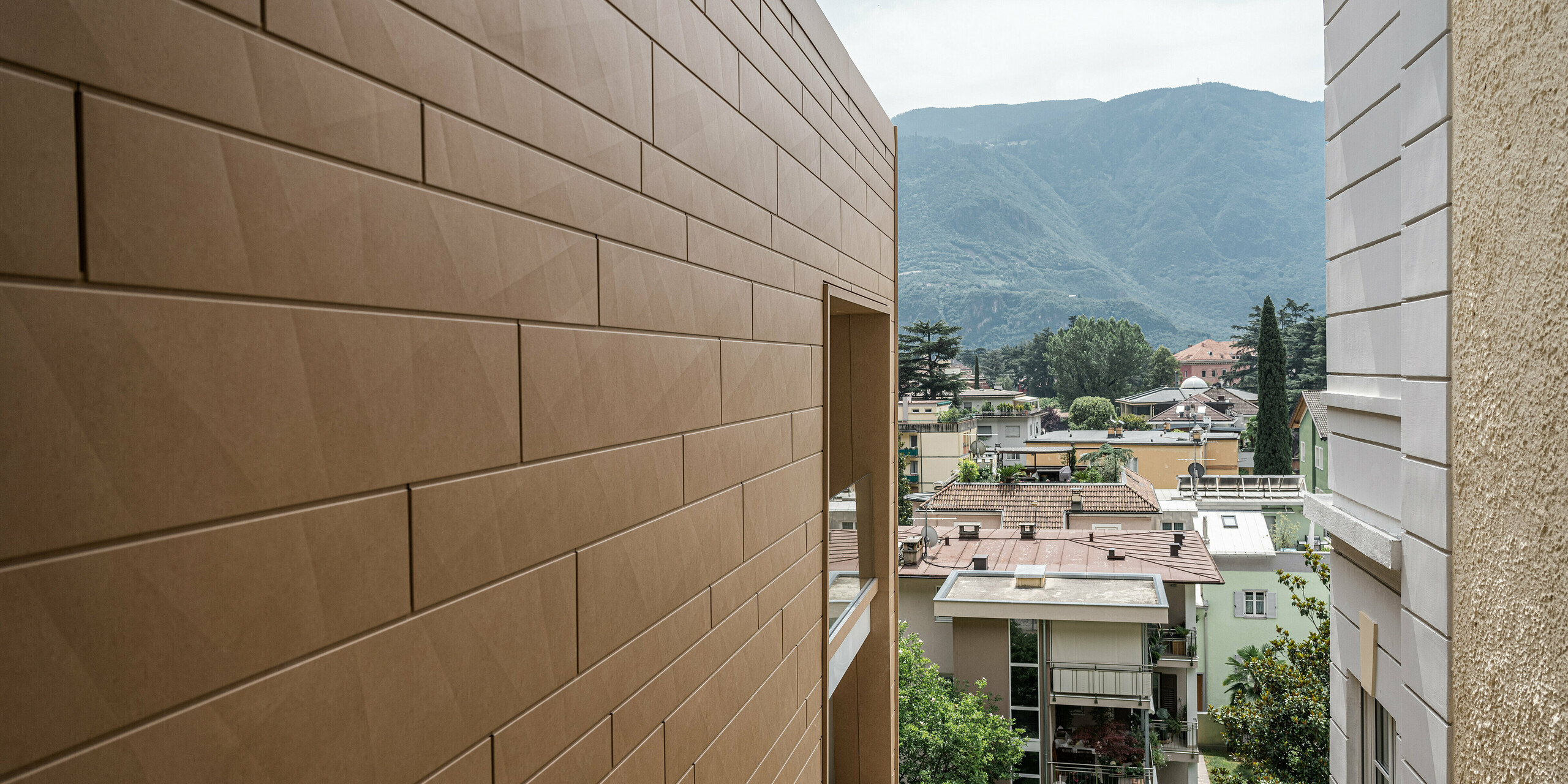 Detailaufnahme der modernen PREFA Siding.X Fassade in P.10 Sandbraun an der Villa Laura in Bozen, Italien. Die harmonisch gefügten Aluminiumelemente bieten eine langlebige und ästhetische Lösung, die sich anmutig in die malerische Bergkulisse Südtirols einfügt. Die Fassade spiegelt die Innovation und Qualität wider, für die PREFA Aluminiumprodukte bekannt sind. Zudem setzt die Gebäudehülle aus Aluminium einen warmen Farbakzent in der urbanen Landschaft.