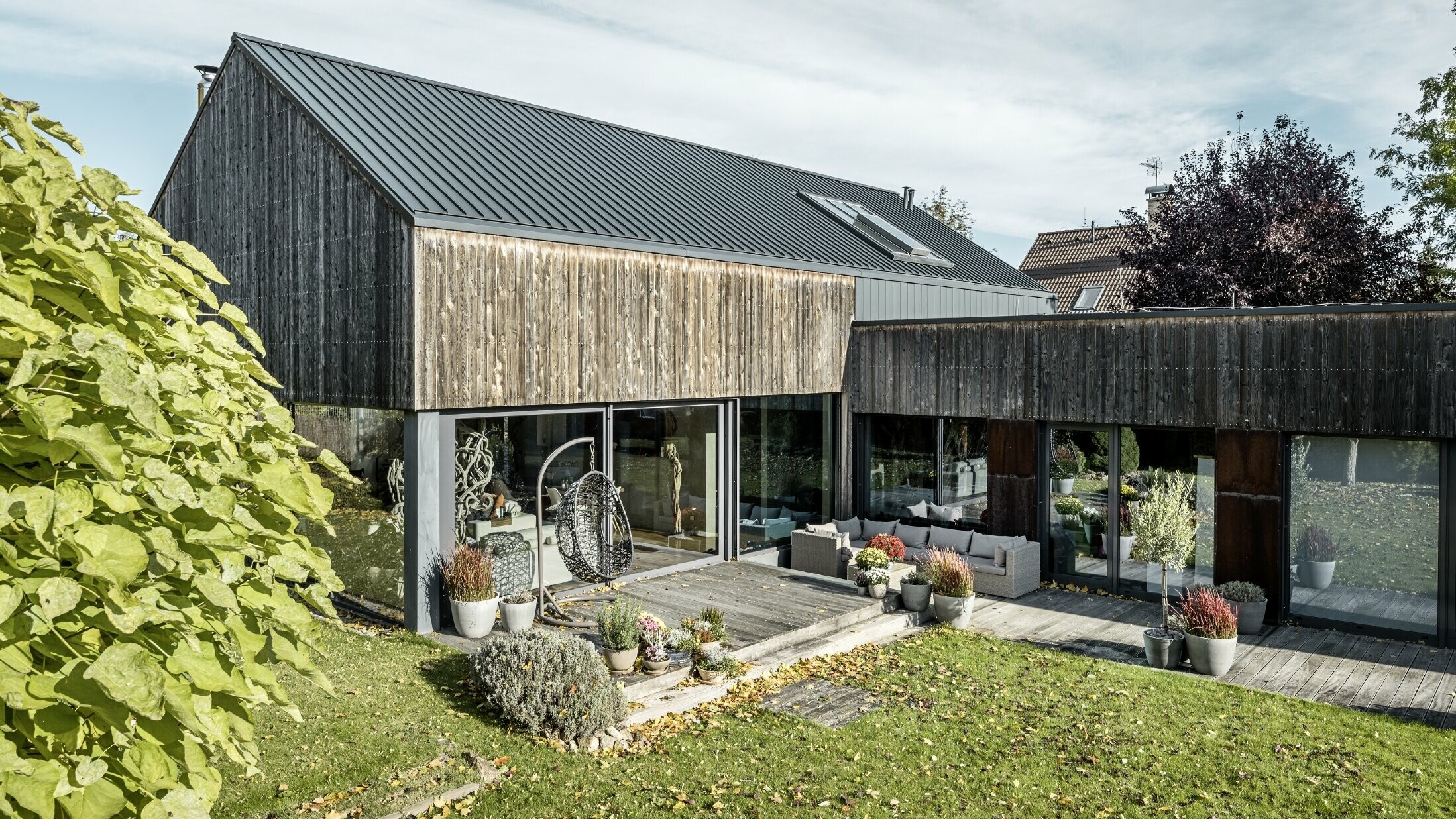 Einfamilienhaus mit Satteldach, eingedeckt mit Doppelstehfalz PREFALZ in Anthrazit und verwitterter Holzfassade. Mit schöner Holzterrasse und großen Fensterflächen im Erdgeschoss.