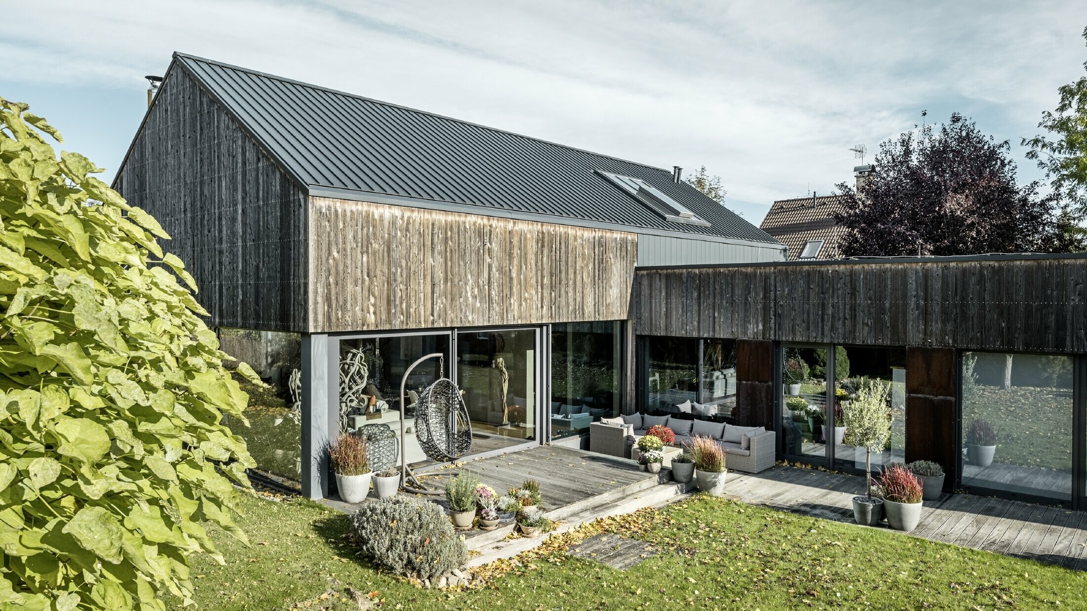 Einfamilienhaus mit Satteldach, eingedeckt mit Doppelstehfalz PREFALZ in Anthrazit und verwitterter Holzfassade. Mit schöner Holzterrasse und großen Fensterflächen im Erdgeschoss.