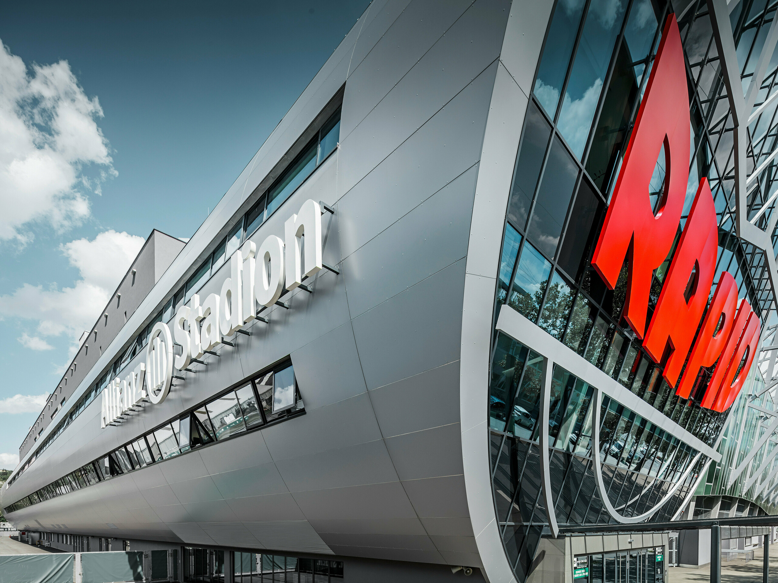 Nahaufnahme der Fassade des Allianz Stadions, Heimat des SK Rapid Wien. Die eindrucksvolle Röhre im Eingangsbereich präsentiert die PREFA Aluminium Verbundplatten in Silbermetallic. Der Blickwinkel unterstreicht die moderne Architektur. Durch den strahlend roten RAPID-Schriftzug und die klare Linienführung der silbernen Platten erhält die Röhre eine visuell beeindruckende Dynamik und Ästhetik. Auf diese Weise wird bereits beim Gang zum Stadion bei allen Fußball-Fans Leidenschaft entfacht.