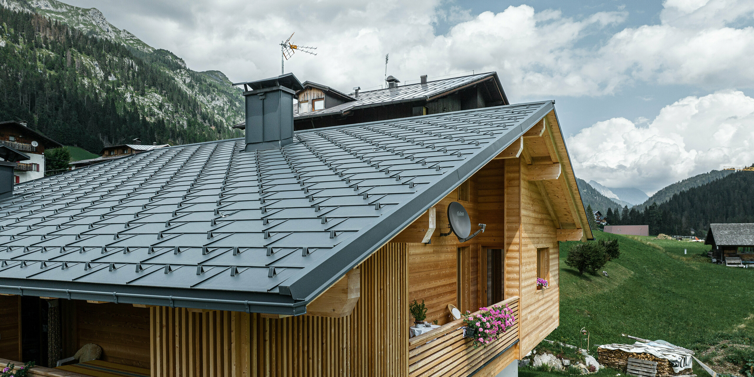 Perspektivische Ansicht des Casa Hoffe in Sappada, Italien, mit langlebigen PREFA Dachplatten R.16 in P.10 Schwarz. Das Dach fügt sich nahtlos in die traditionelle Holzbauweise ein und bietet einen ästhetischen Kontrast, der durch die alpine Landschaft ergänzt wird. Die Kombination aus dem schwarzen PREFA Dachsystem und der natürlichen Holzfassade repräsentiert eine Symbiose aus Beständigkeit, Qualität und alpinem Charme.