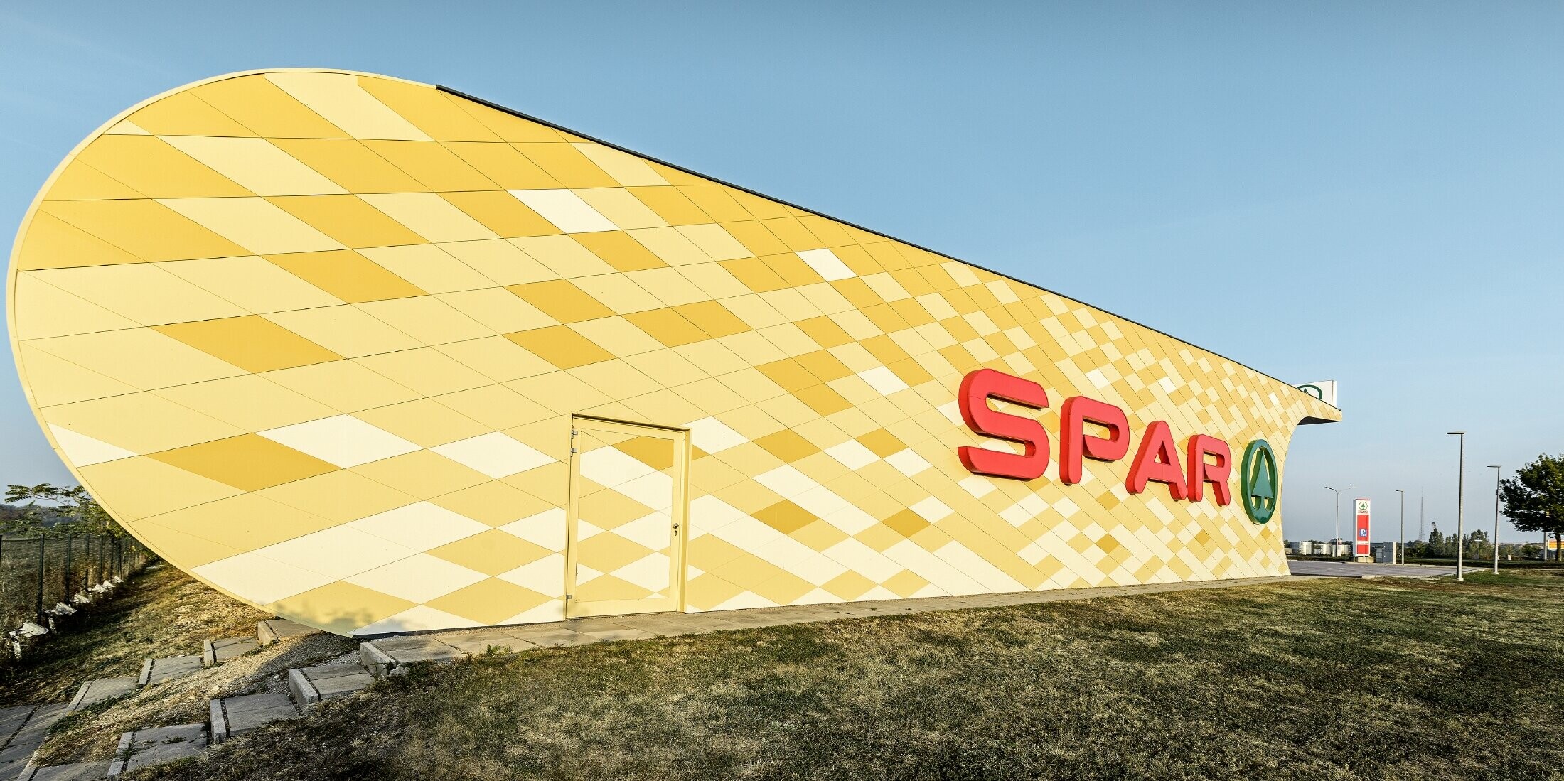 Spar Filiale mit einer Aluminiumfassade in gelb-orangen Karos und Spar Logo