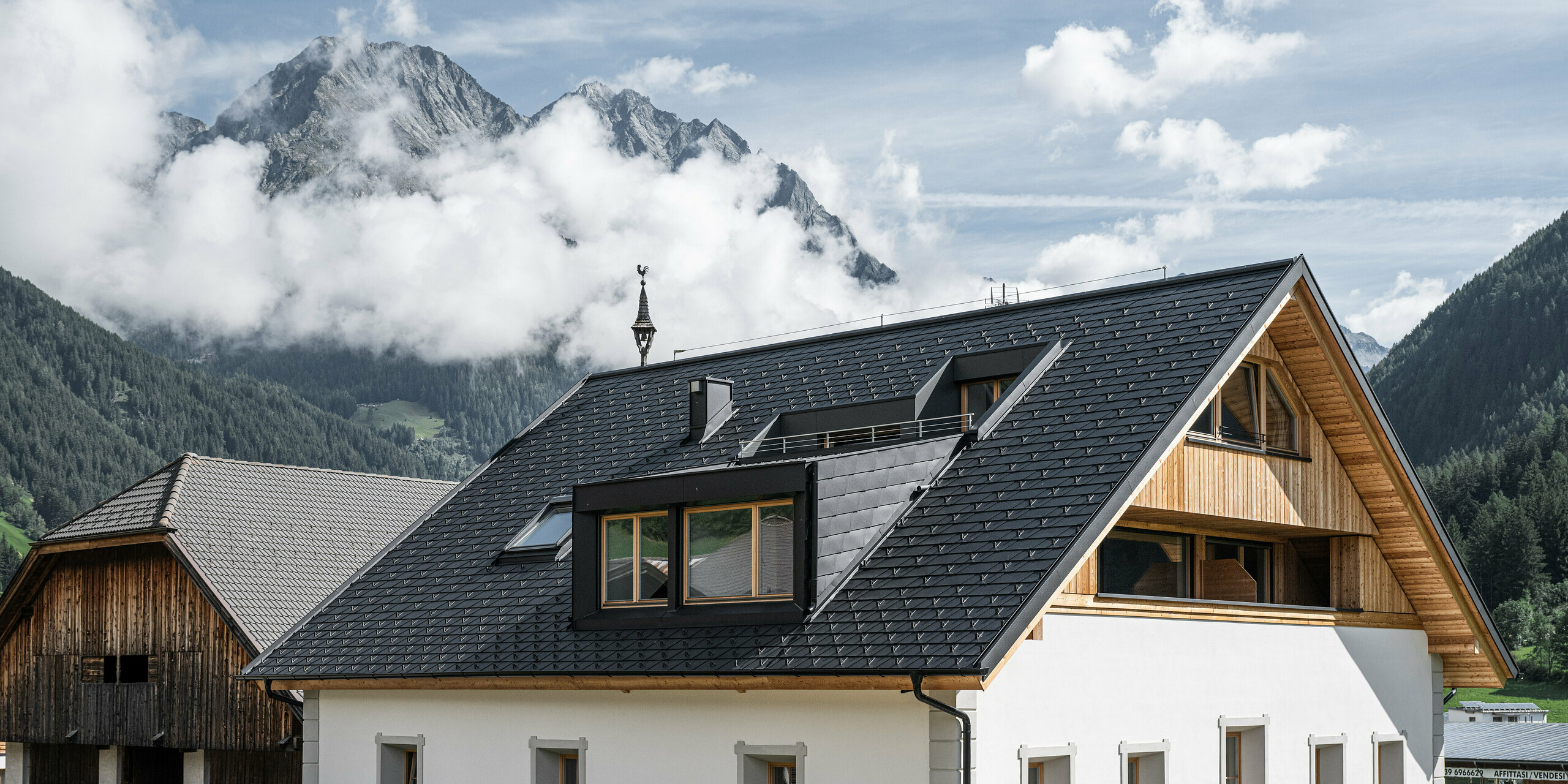 Detailansicht des wind- und wetterfesten PREFA Dachsystems. Das Satteldach des Außerwegerhofs in Südtirol wurde mit robusten PREAF DS.19 Dachschindeln in P.10 anthrazit eingedeckt. Die ästhetische Dachgestaltung ist umgeben von der beeindruckenden Bergkulisse des Antholzertals.