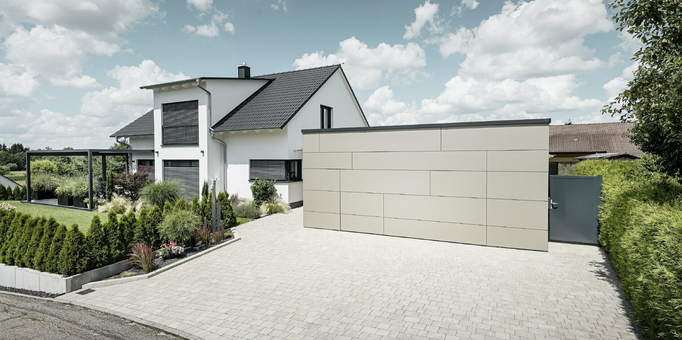 Die Garage des Einfamilienhauses ist an der Fassade komplett mit der Aluminium Verbundplatte in Bronze verkleidet. Auch das Garagentor ist mit den Fugen nicht erkennbar. Davor ist eine großzügige Einfahrt. 