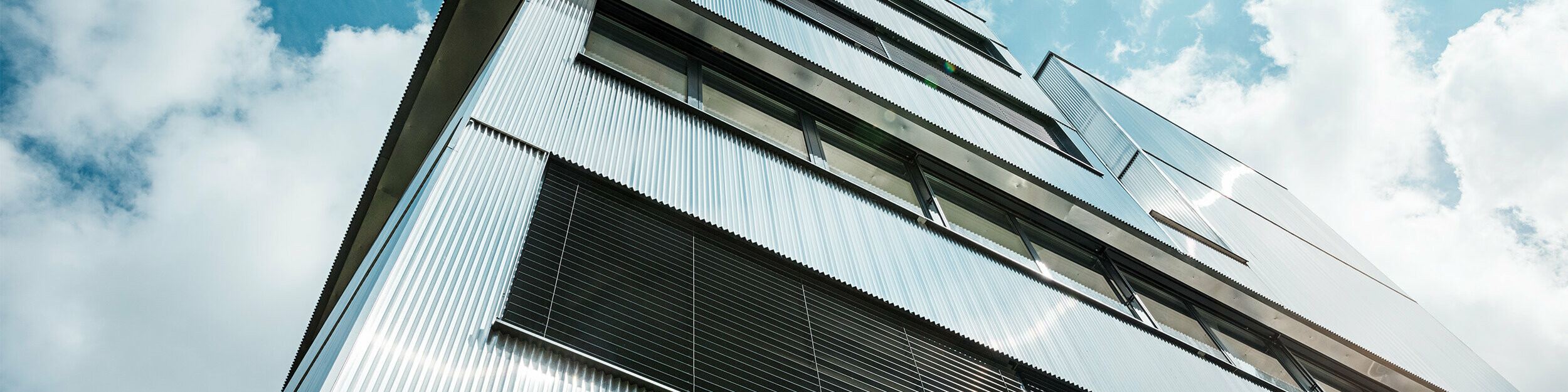 Nahaufnahme der Fassade der Musikschule in Bjevolar mit dem PREFA Zackenprofil. Die Fassade besteht aus einer Kombination von schwarzen und naturblanken Oberflächen, die in der Sonne glänzen und das moderne Design betonen.