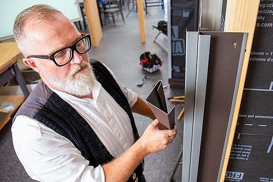 Der PREFA Experte hält die Abdeckungen für die Innen- und Außenecke	in der Hand, die er an diese anschließend anbringt.