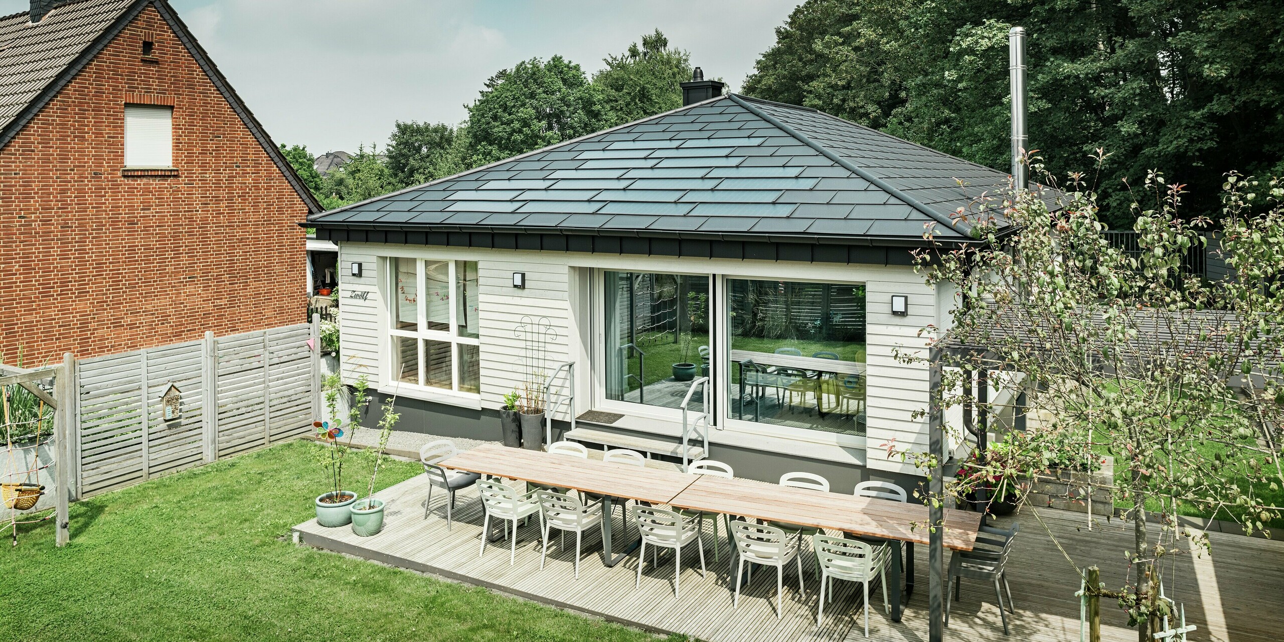 Sanierter Bungalow in Rommerskirchen mit großzügiger Terrasse, einladenden Fensterflächen und hochwertigem PREFA Aluminiumdach. PREFA Solardachplatten erzeugen nachhaltig Strom und die Dachplatten R.16 in P.10 schwarz bieten optimalen Schutz und eine elegante Optik. Funktionalität und modernes Design perfekt vereint. Vor dem Einfamilienhaus befindet sich ein gepflegter Garten mit einladendem Sitzplatz auf der Terrasse.