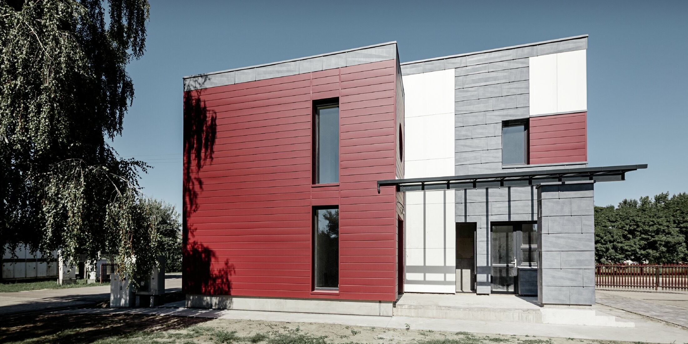 Modernes Bürogebäude mit einer geteilten Fassade in rot, steingrau und weiß mit Aluminiumprodukten Sidings, Fassadenpaneel FX.12 und Aluminium Verbundplatte von PREFA