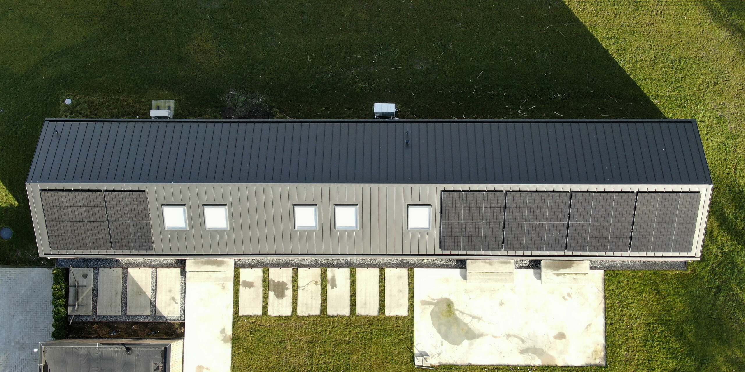 Vogelperspektive eines modernen Einfamilienhauses in Uithoorn, Niederlande, mit PREFALZ Winkelstehfalz-Eindeckung in Schwarzgrau und integrierter Photovoltaik-Anlage. Das Bild zeigt die effiziente Nutzung des Dachs für Solarmodule sowie die robuste und wetterbeständige Bauweise des hochwertigen Aluminiumdachs. Ideal für nachhaltige Bauprojekte, die erneuerbare Energien und modernes Design integrieren.