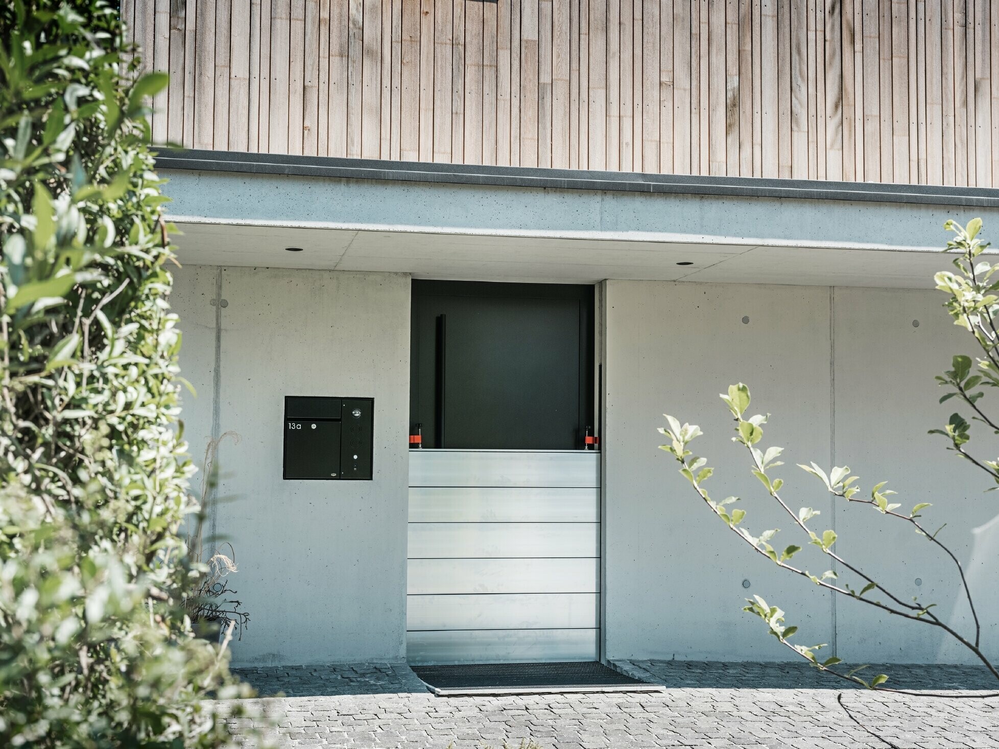 Vor der Eingangstür eines Einfamilienhauses mit Holzfassade ist der PREFA Hochwasserschutz aufgebaut. 