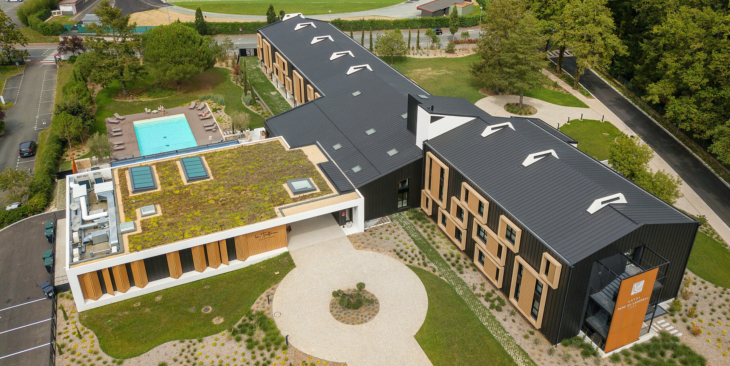 Vogelperspektive des Hôtel Parc du Landreau in Les Herbiers, Frankreich, mit dem PREFALZ Dach- und Fassadensystem in Schwarzgrau. Die Fassade ist mit modernen Holzrahmen um die Fenster gestaltet, während der Swimmingpool den Außenbereich für die Gäste aufwertet. Das Hotel verbindet nachhaltiges Bauen mit ästhetischem Design.