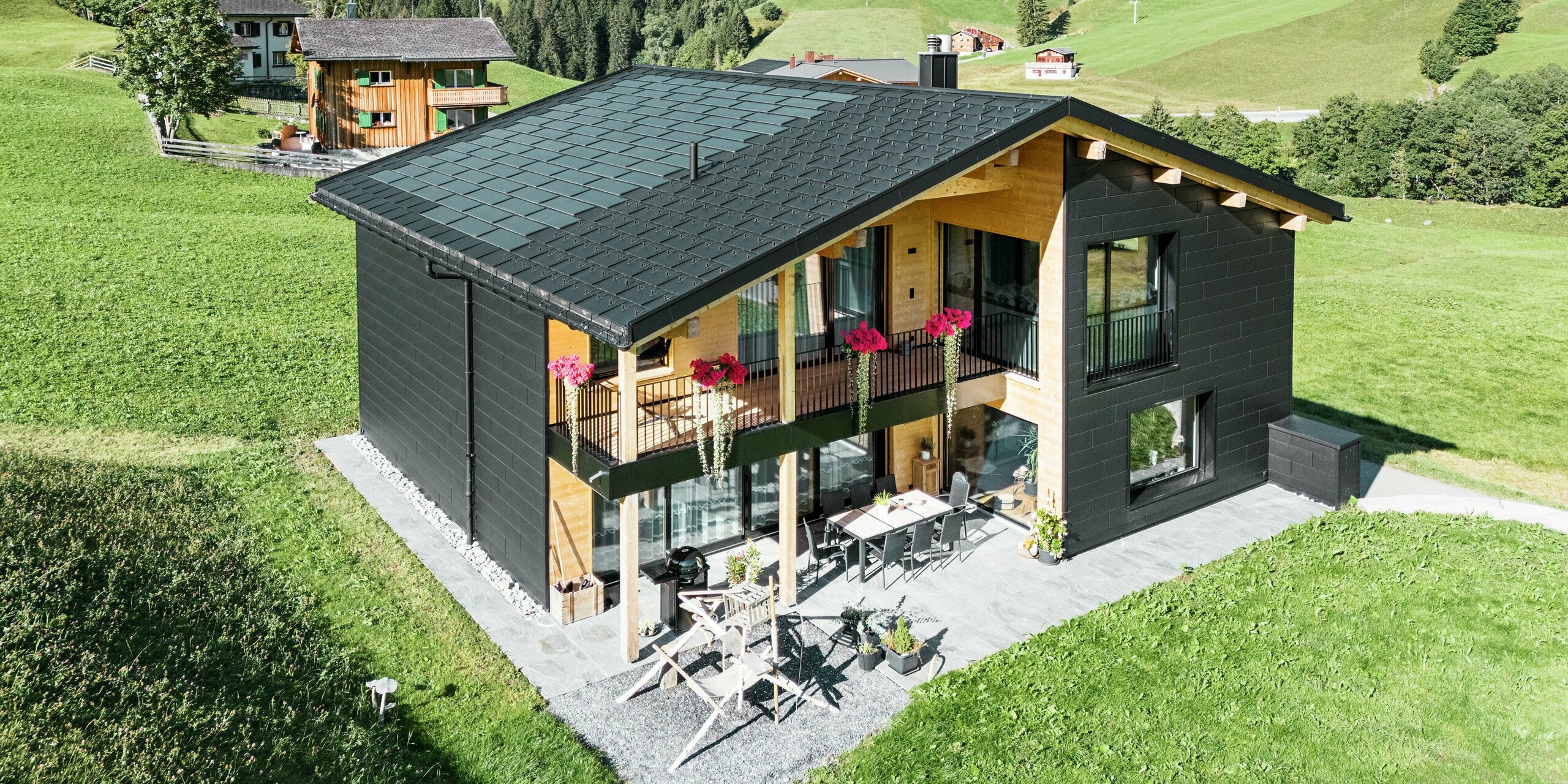 Das elegante Einfamilienhaus in der hügeligen Umgebung von Ascharina (Schweiz) zeigt, wie sich Aluminium und Holz perfekt kombinieren lassen. Die robusten PREFA Siding.X Fassadenpaneele in P.10 Schwarz harmonieren mit dem Dach aus PREFA Solardachplatten und Dachplatten R.16 in der gleichen Farbbeschichtung. Die langlebige Aluminiumhülle schützt das Gebäude zuverlässig vor den Herausforderungen des alpinen Klimas.