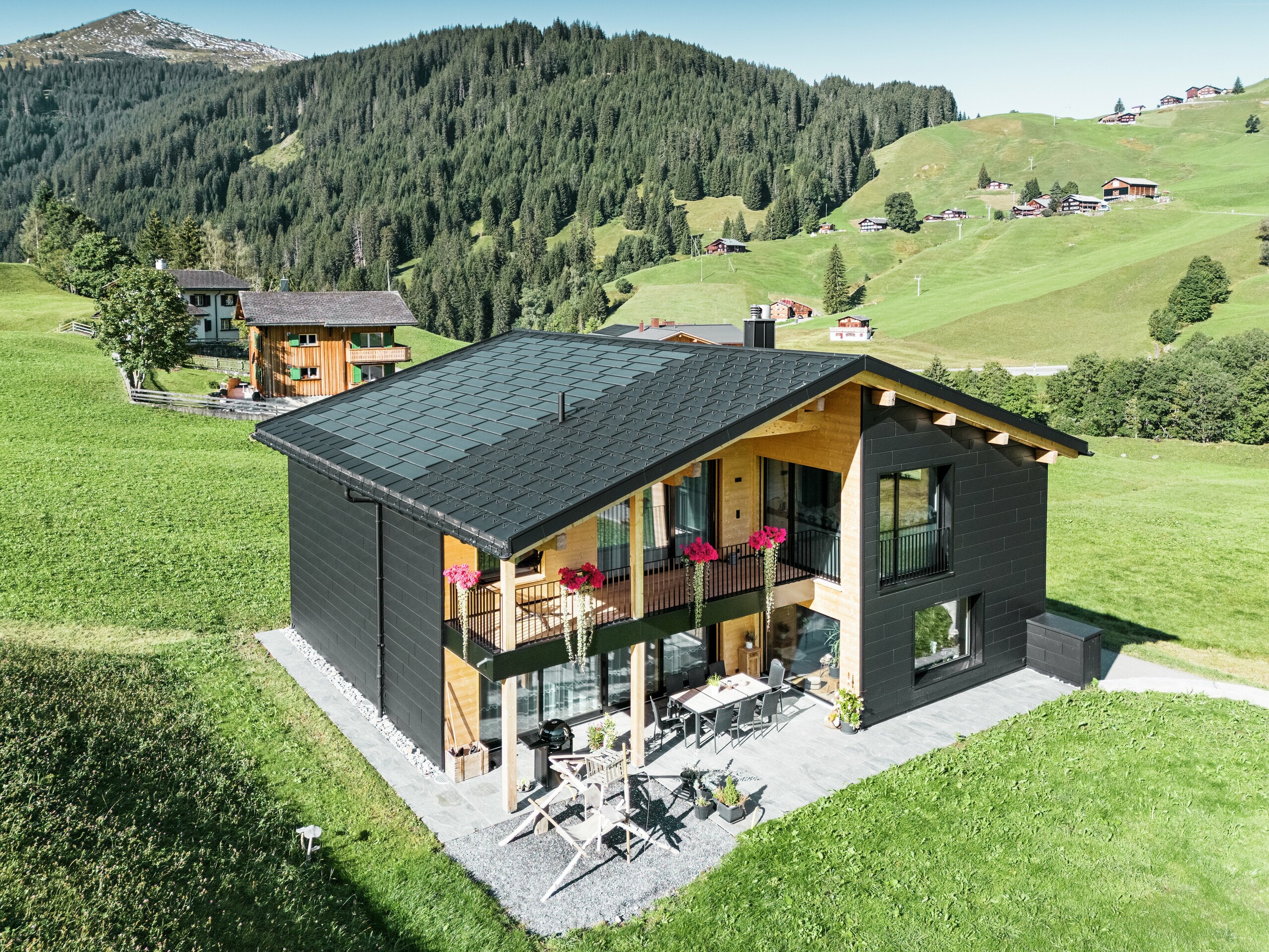 Das elegante Einfamilienhaus in der hügeligen Umgebung von Ascharina (Schweiz) zeigt, wie sich Aluminium und Holz perfekt kombinieren lassen. Die robusten PREFA Siding.X Fassadenpaneele in P.10 Schwarz harmonieren mit dem Dach aus PREFA Solardachplatten und Dachplatten R.16 in der gleichen Farbbeschichtung. Die langlebige Aluminiumhülle schützt das Gebäude zuverlässig vor den Herausforderungen des alpinen Klimas.