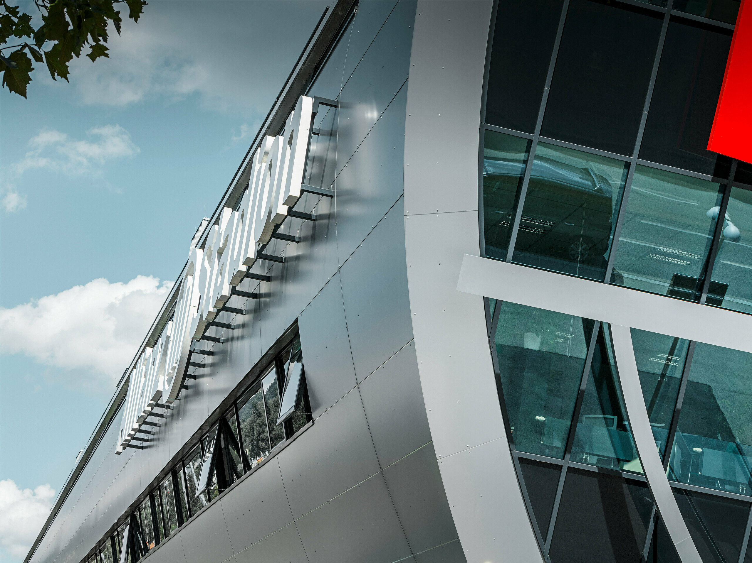 Detailaufnahme der Fassadenverkleidung des Allianz Stadions, der Heimstätte des SK Rapid Wien. Der Fokus des Bildes richtet sich auf die glänzende Fassade aus PREFA Aluminium Verbundplatten in Silbermetallic. Am Bildrand sind der Name des Bauwerks „Allianz Stadion“ sowie die großen Glasflächen und ein Ansatz des leuchtend roten Logos von Rapid Wien zu erkennen.