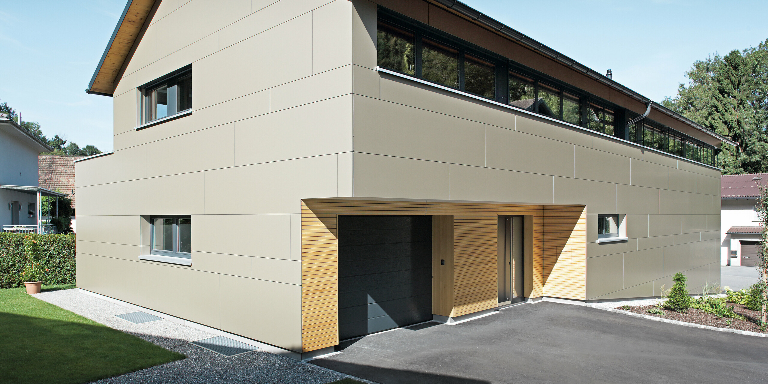 Elegantes Einfamilienhaus in Hohenems, ausgestattet mit einem PREFA Komplettsystem. Die Fassade besteht aus Aluminium Verbundplatten in Bronzemetallic, die einen modernen und klaren Look schaffen, während die Holzelemente am Garageneingang Wärme und Natürlichkeit ausstrahlen. Das Dach ist mit PREFA Dachplatten in P.10 Anthrazit gedeckt, die zusammen mit der Fassade ein architektonisches Gesamtkonzept bilden und das Haus effektiv schützen.