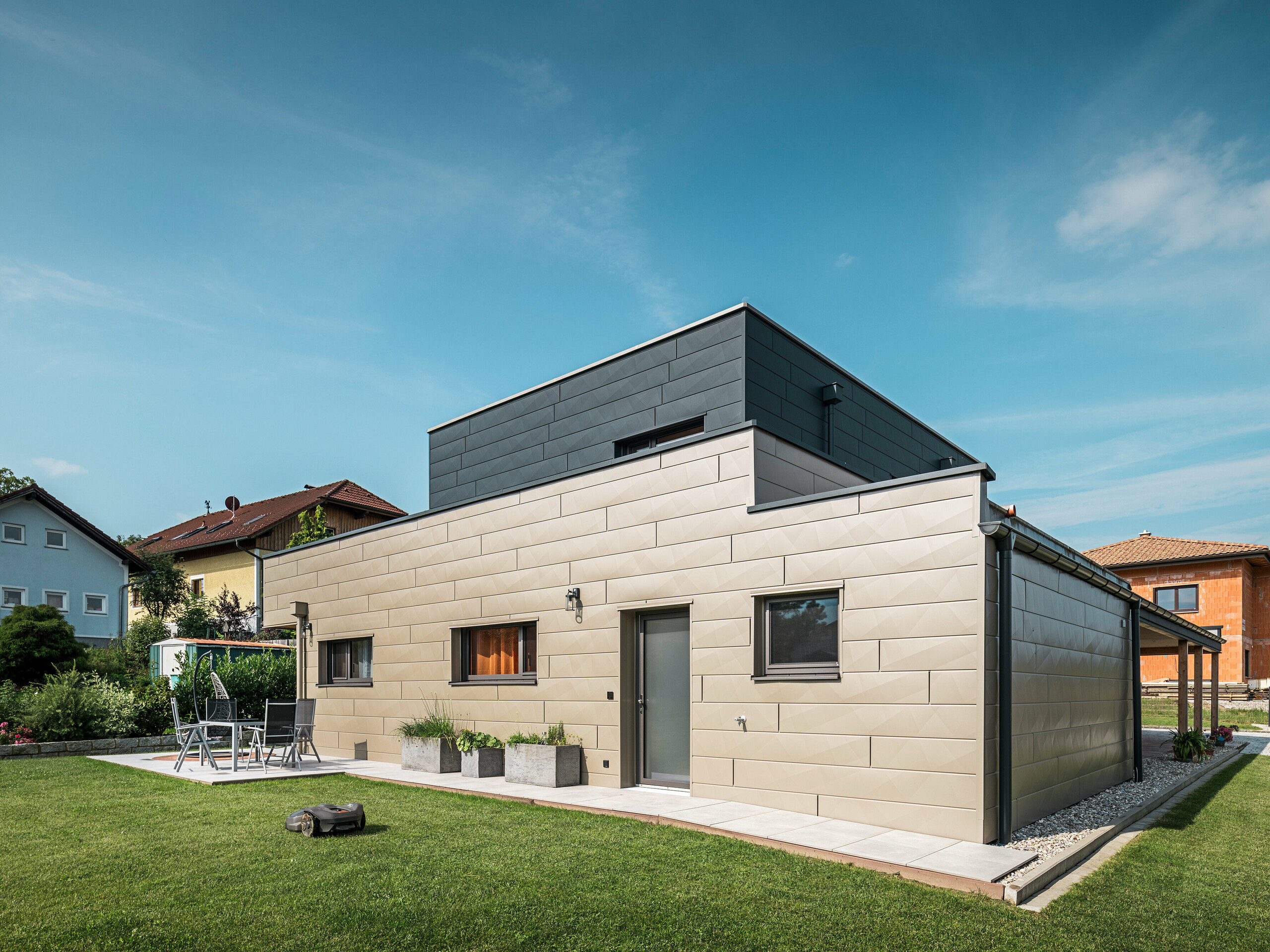 Modernes Einfamilienhaus in Wippenham, Österreich, mit zweifarbiger PREFA Aluminiumfassade in Bronze und Anthrazit. Die Fassade ist mit Siding.X Fassadenpaneelen gestaltet, die für eine elegante und zeitgemäße Optik sorgen. Die integrierte PREFA Dachentwässerung mit Wasserfangkasten und Ablaufrohr sowie eine gepflegte Gartenanlage mit Terrasse betonen das moderne Design des Hauses.