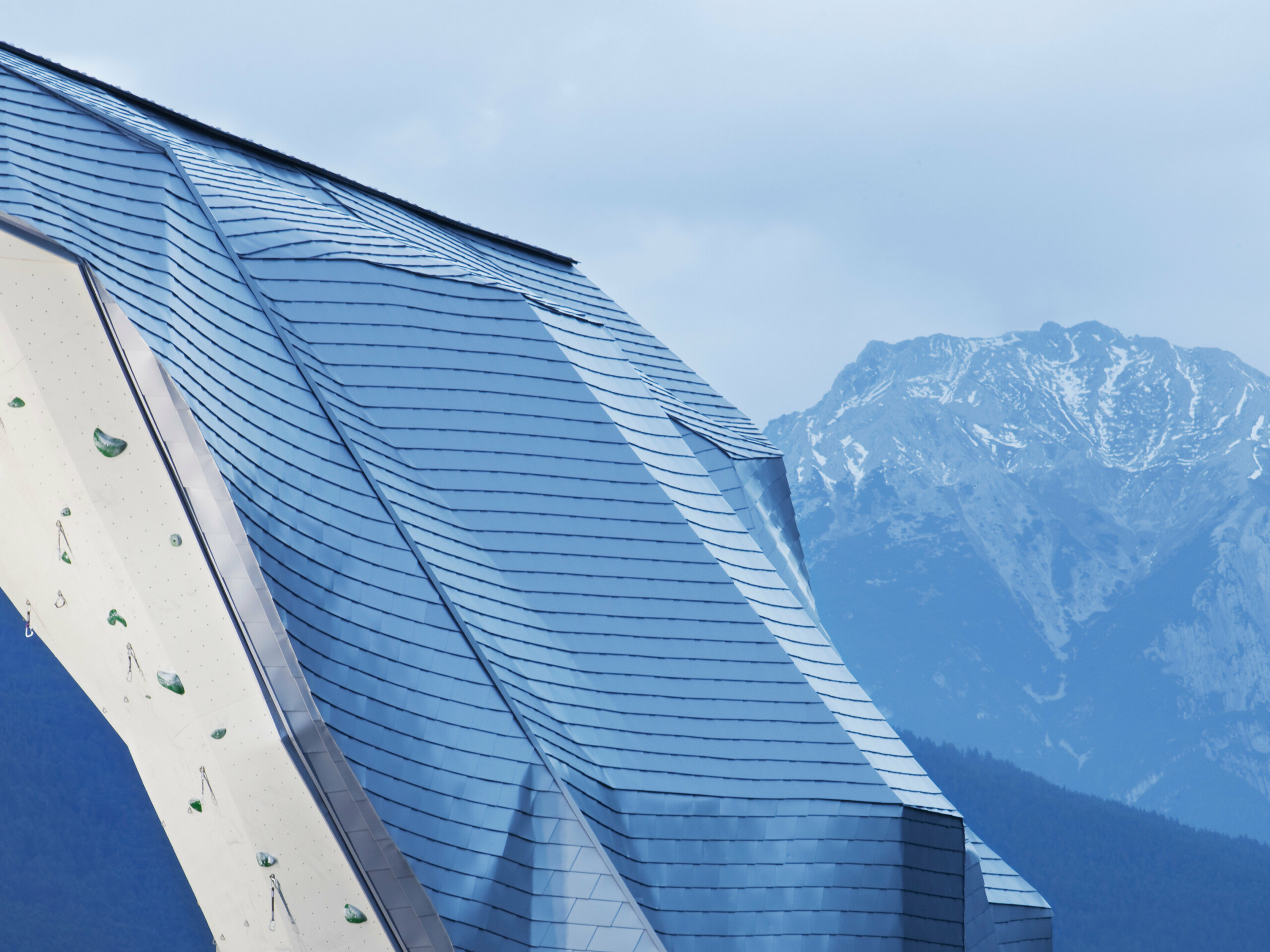 Der Kletterturm in Imst mit einer Hülle aus Aluminium in Silbermetallic und einem schönen Bergpanorama im Hintergrund