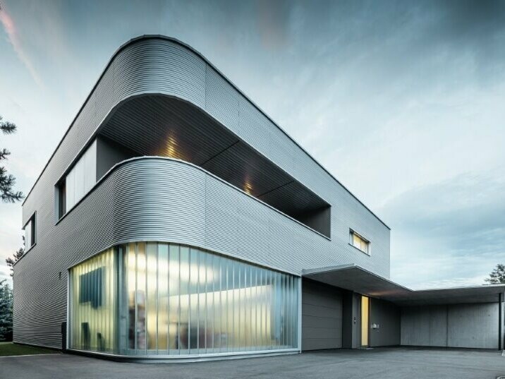 seitliche Ansicht des Hauses in Leonding in Linz bei Dämmerung. Der Himmel ist leicht bewölkt. Das Haus wurde mit der PREFA Profilwelle natureloxiert verkleidet.