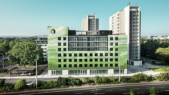 Seitenansicht des Wohn- und Geschäftshauses "Pick-Nick" am Straßburger Platz in Dresden mit einer auffälligen PREFA Fassade aus robustem Aluminium. Das moderne Gebäude mit seinen klaren Linien und großflächigen Fenstern integriert sich in das urbane Umfeld zwischen Wohnhochhäusern und Grünflächen. Das prägnante Design setzt architektonische Akzente.