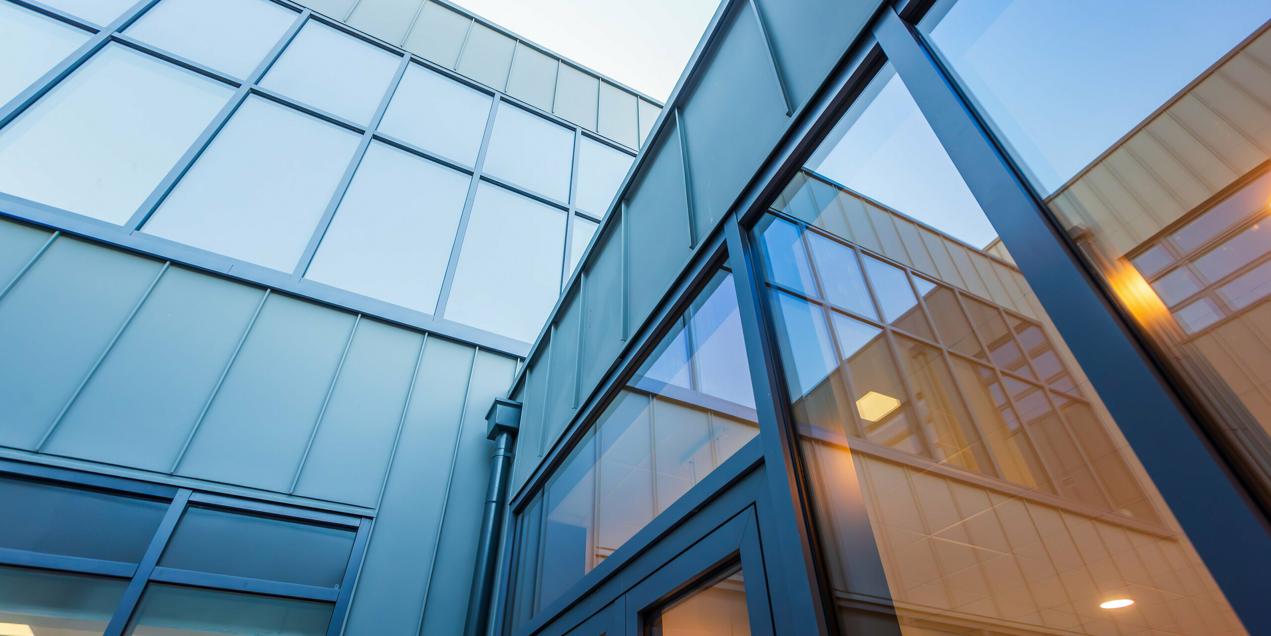 Froschperspektive auf die moderne PREFALZ Aluminiumfassade in P.10 Hellgrau der Scoil Mhuire Naofa in Carrigtwohill, Irland. Große Fensterflächen und präzise Stehfalzbahnen unterstreichen die zeitgenössische Architektur und sorgen für ein lichtdurchflutetes, elegantes Design.