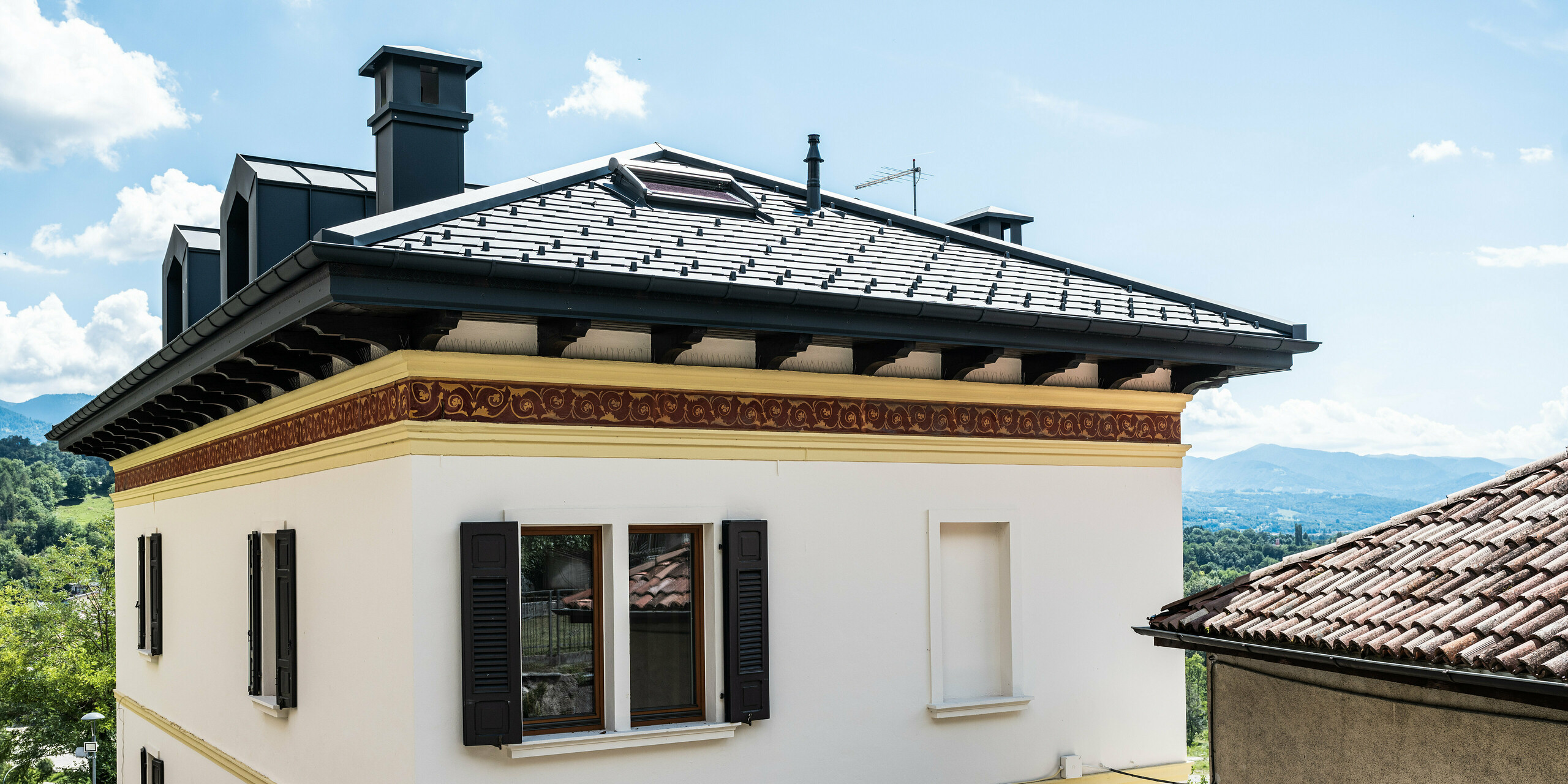 Restauriertes Gebäude in Belluno, gekennzeichnet durch ein PREFA Dach mit anthrazitfarbenen Aluminiumschindeln, die die strukturelle Integrität wahren. Die klassische Fassade mit dekorativen Frieselementen fügt sich nahtlos in die malerische italienische Landschaft ein und wird durch das moderne, langlebige und stilvolle PREFA Dachsystem in der Farbe P.10 Anthrazit abgerundet.