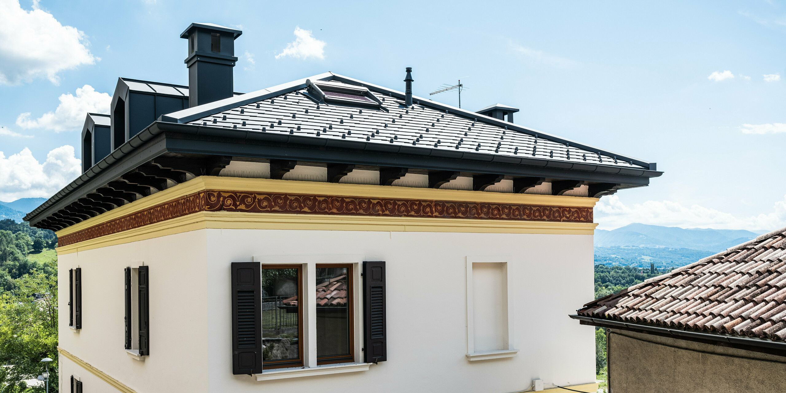 Restauriertes Gebäude in Belluno, gekennzeichnet durch ein PREFA Dach mit anthrazitfarbenen Aluminiumschindeln, die die strukturelle Integrität wahren. Die klassische Fassade mit dekorativen Frieselementen fügt sich nahtlos in die malerische italienische Landschaft ein und wird durch das moderne, langlebige und stilvolle PREFA Dachsystem in der Farbe P.10 Anthrazit abgerundet.