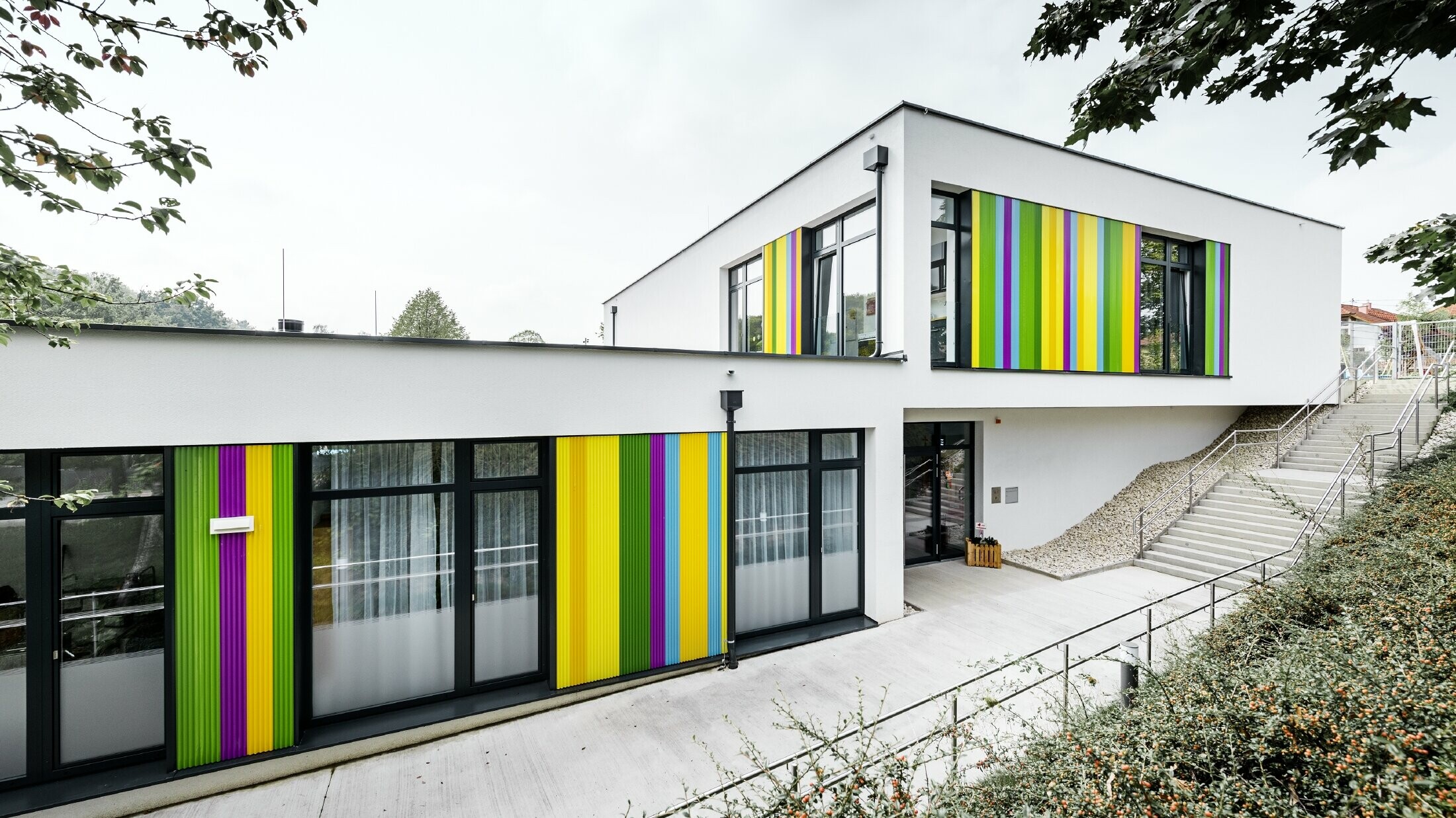 Bunte Fassadenelemente von PREFA für den Kindergarten in Hargelsberg. Das Gebäude hat ein Flachdach und große, bodentiefe Fenster.