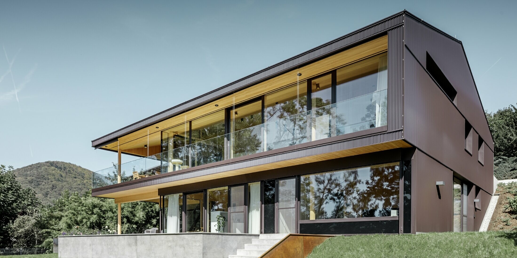 Modernes Einfamilienhaus mit großen Fenstern auf der Gartenseite, die Fassade wurde mit dem PREFA Zackenprofil in dunklem Braun bekleidet.