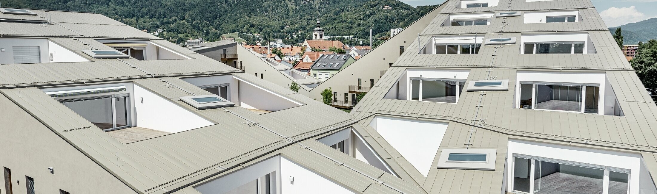 lang gezogene Wohnhausanlage in Graz mit flachen Dachflächen und integrierten Terrassen und großflächigen Fenstern mit einem Prefalzdach in der Sonderfarbe broncemetallic