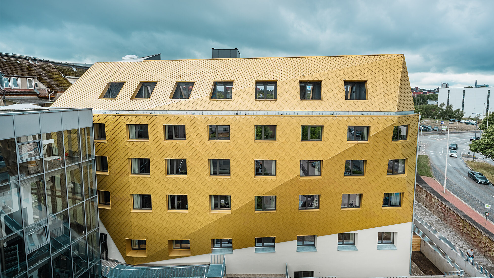 Die asymmetrische Aluminiumfassade von der Seite, rundherum die gebaute Umgebung.