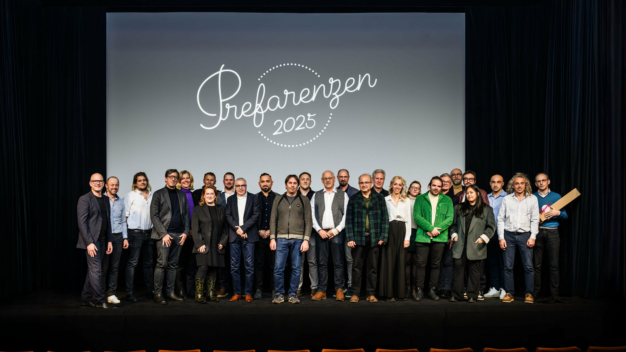 Gruppenfoto bei der PREFARENZEN-Premiere 2025 im Stadtkino Wien: Jürgen Jungmair, Marketingleiter von PREFA, mit den Mitwirkenden und Gästen vor dem Logo der Veranstaltung ‚Prefarenzen 2025‘ auf der Leinwand. Die Teilnehmer:innen repräsentieren Architektur, Planung, Verarbeitung und Medien aus ganz Europa.