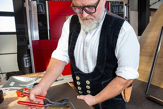 Dieses Bild zeigt den PREFA Techniker mit einer Falzzange mit roten Griffen. Diese verwendet er zur Herstellung der Rückkantung. 