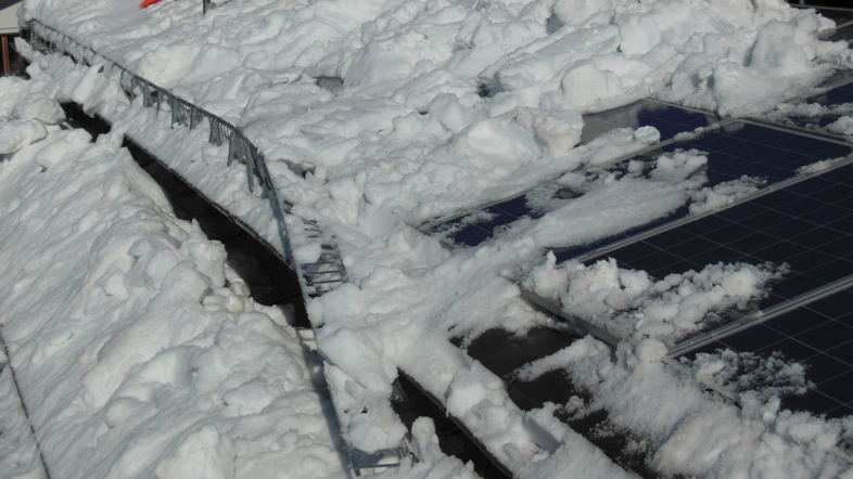 Ein schneebedecktes Dach, auf dem ein beschädigtes Schneerechensystem sichtbar ist. Der Schnee hat sich unkontrolliert auf dem Dach verteilt, was zu potenziellen Schäden und Sicherheitsrisiken führen kann. Das Bild zeigt die Wichtigkeit eines intakten Schneeschutzsystems, insbesondere in schneereichen Regionen, um die Dachkonstruktion und umliegende Bereiche zu schützen.