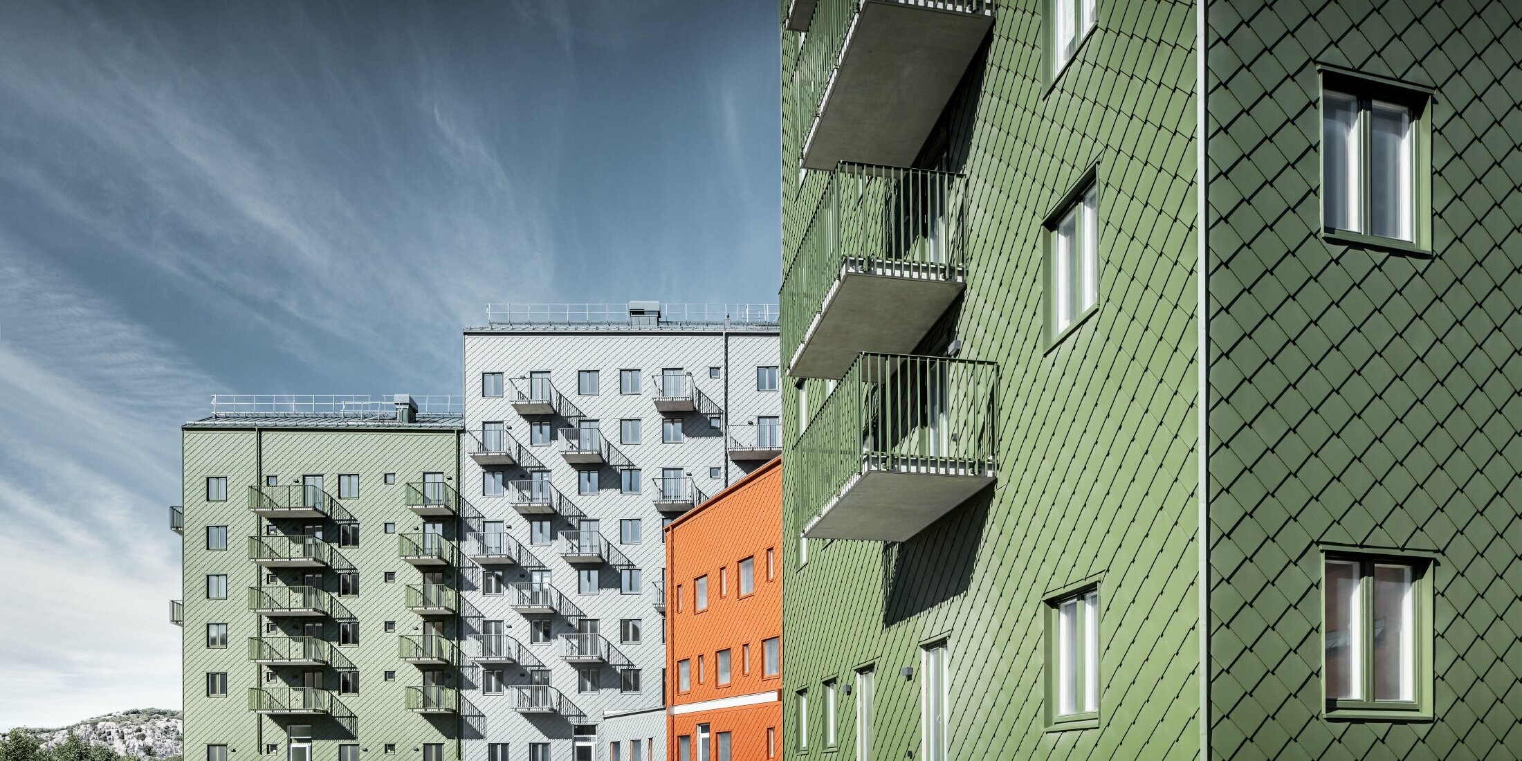 Mehrere Wohnhäuser nebeneinander, eingekleidet mit der PREFA Wandraute 29 × 29 in den Farben Ziegelrot, Olivgrün und Hellgrau.