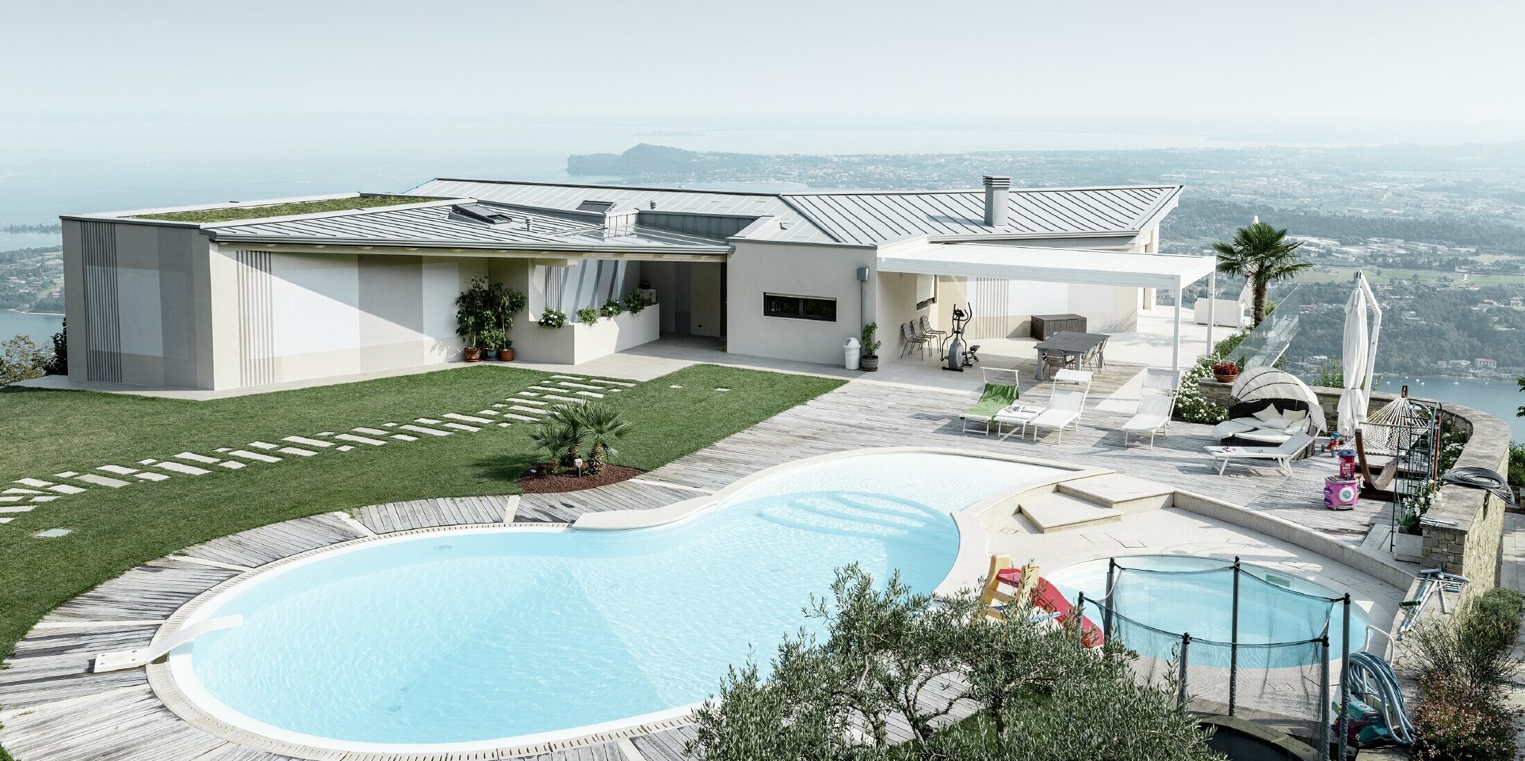 Anwesen auf einer Anhöhe mit weiten Blick in die Landschaft, großer Terrasse und Swimmingpool mit einem Stehfalzdach in patina grau 