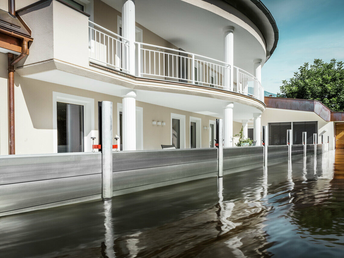 Zu sehen ist ein Einfamilienhaus mit Balkon. Durch den PREFA Hochwasserschutz ist das Haus vor dem bereits steigenden Hochwasser geschützt.