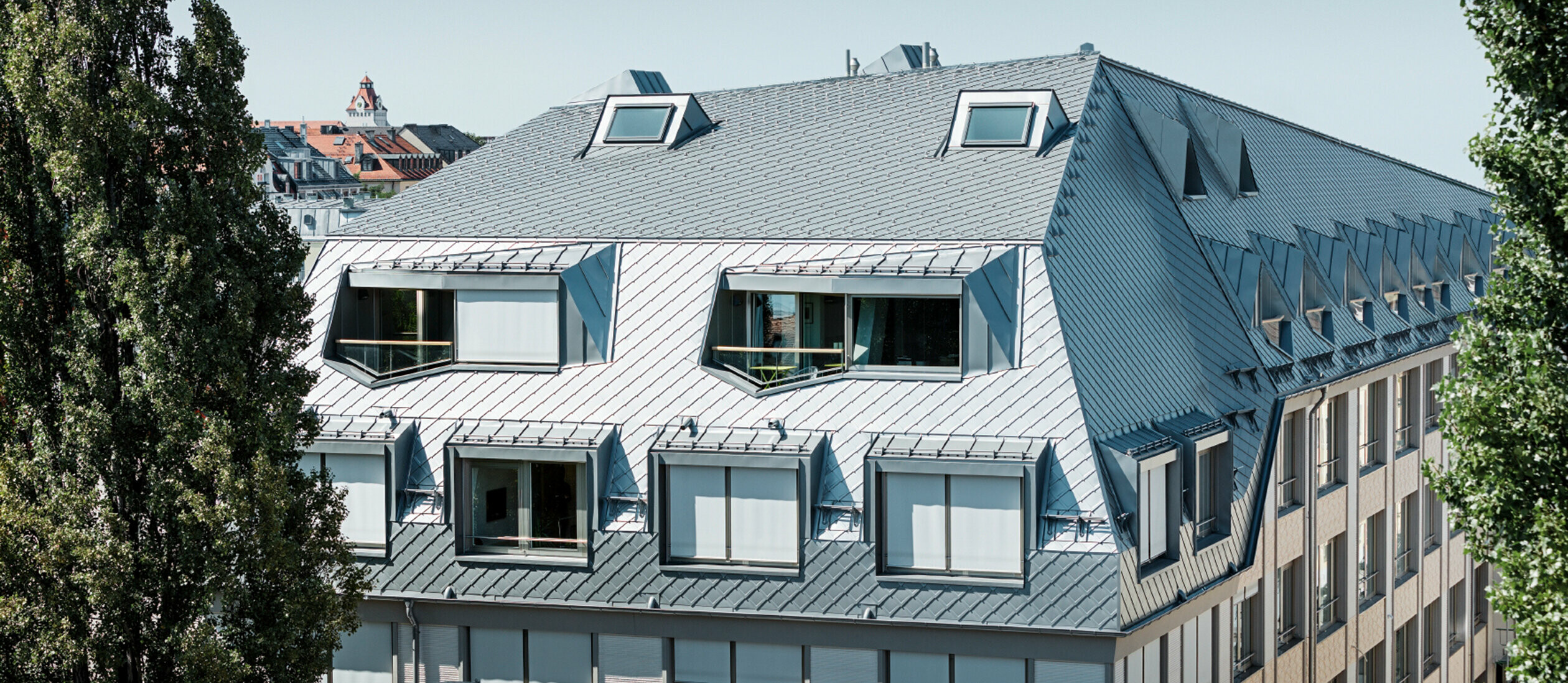 Dachausbau eines Walmdaches in derLeopoldstraße/Ecke Hohenzollernstraße in München. Viele Loggiaausschnitte und Fensterausschnitte werden von der PREFA Dachraute eingekleidet.