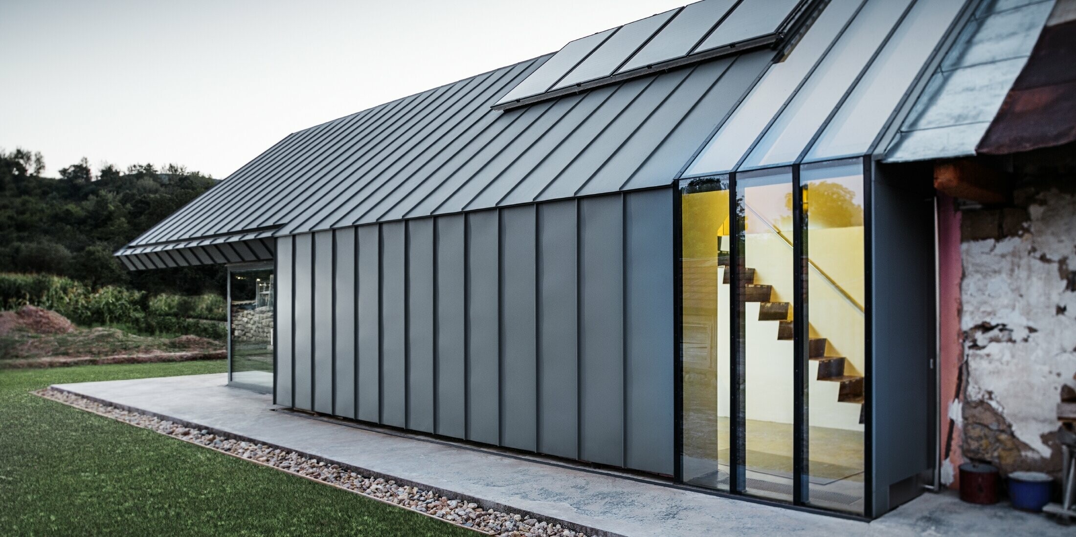 modernes neues Architektenbüro und Einfamilienhaus im Anschluss an ein altes Bauernhaus mit Steinfassade, verkleidet mit Stehfalz und Winkelstehfalz von PREFA in Hellgrau