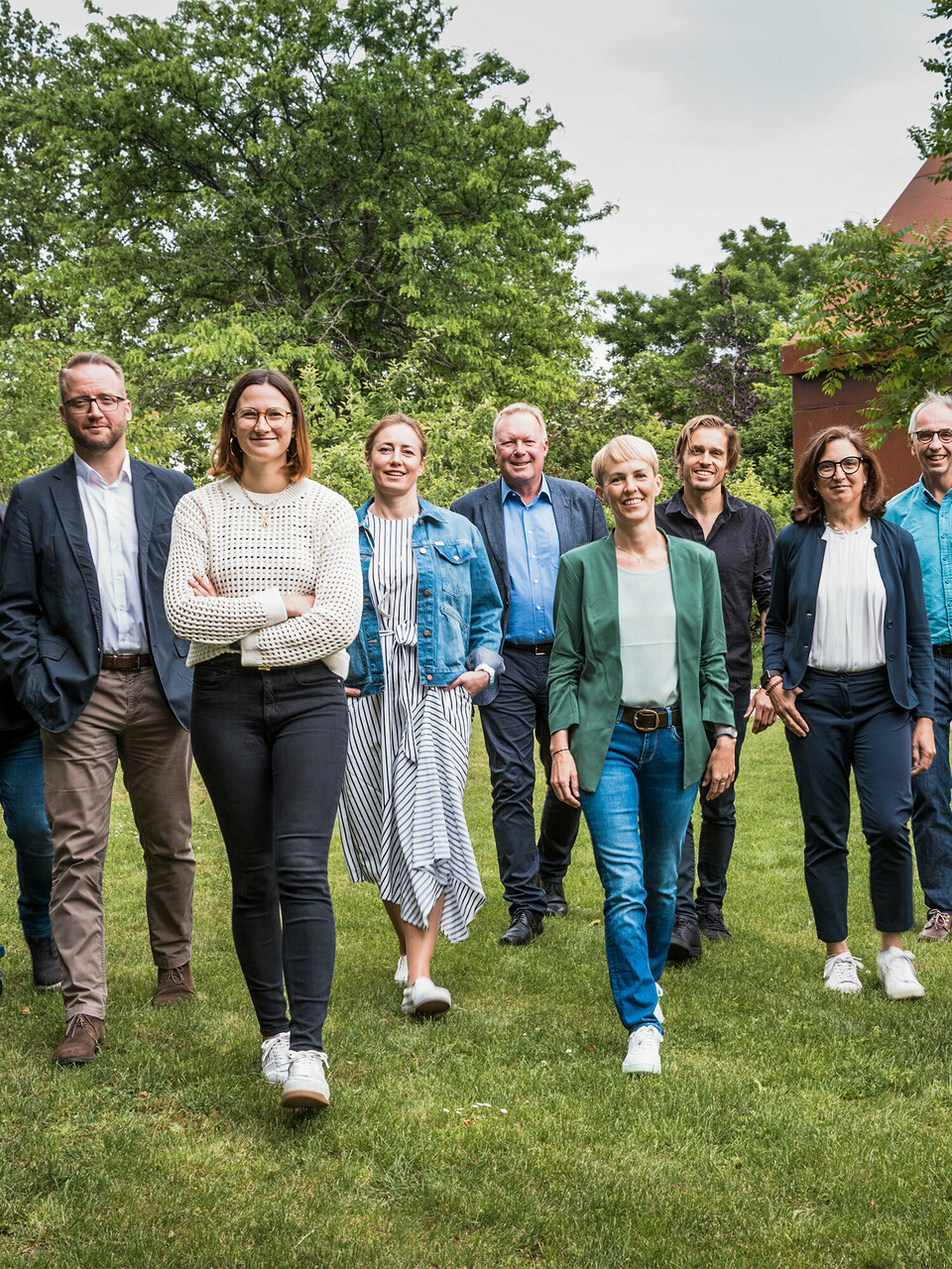 Gruppe von Expert:innen und Architekt:innen beim PREFARENZEN 2025 Dialog: Die Jury besteht aus zehn Architekt:innen und PREFA Expert:innen, die gemeinsam auf einer grünen Wiese vor der Residenz Velich im burgenländischen Seewinkel in eine gemeinsame Richtung gehen. Sie lächeln und gehen frontal auf die Kamera zu. Im Hintergrund ist die üppige Vegetation der Umgebung zu sehen. Das Bild entstand bevor die Jury die spannendsten Architekturobjekte für die PREFA Architekturplattform 2025 auswählte. Beim PREFARENZEN Dialog im Mai 2024 lag der Fokus auf der Funktionalität und Einfachheit sowie dem Mehrwert moderner Architekturobjekte. Auf dem Bild zu sehen v. l. n. r.: Thomas Heil (Co-Gründer, dreiplus Architekten), Jürgen Haller (Baumeister, Jürgen Haller GmbH), Christian Wirth (Leiter Objektberatung, PREFA Österreich), Chiara Desbordes (Head of Content, Architektur Aktuell), Paulina Frey (Marketingleiterin, PREFA Schweiz), Gerald Krebs (Objektberater, PREFA Österreich), Veronika Roll (Marketing PREFA Österreich), Daniel Luckeneder (Associate Partner, laac zt gmbh), Patricia Ezcurra (Architektin, wwa Architekten), Wolfgang Croce (Croce & Wir, Graz), Bettina Almeida (Kommunikationsmanagement, PREFA), Jürgen Jungmair (Marketingleiter International, PREFA).