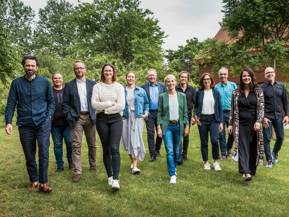 Gruppe von Expert:innen und Architekt:innen beim PREFARENZEN 2025 Dialog: Die Jury besteht aus zehn Architekt:innen und PREFA Expert:innen, die gemeinsam auf einer grünen Wiese vor der Residenz Velich im burgenländischen Seewinkel in eine gemeinsame Richtung gehen. Sie lächeln und gehen frontal auf die Kamera zu. Im Hintergrund ist die üppige Vegetation der Umgebung zu sehen. Das Bild entstand bevor die Jury die spannendsten Architekturobjekte für die PREFA Architekturplattform 2025 auswählte. Beim PREFARENZEN Dialog im Mai 2024 lag der Fokus auf der Funktionalität und Einfachheit sowie dem Mehrwert moderner Architekturobjekte. Auf dem Bild zu sehen v. l. n. r.: Thomas Heil (Co-Gründer, dreiplus Architekten), Jürgen Haller (Baumeister, Jürgen Haller GmbH), Christian Wirth (Leiter Objektberatung, PREFA Österreich), Chiara Desbordes (Head of Content, Architektur Aktuell), Paulina Frey (Marketingleiterin, PREFA Schweiz), Gerald Krebs (Objektberater, PREFA Österreich), Veronika Roll (Marketing PREFA Österreich), Daniel Luckeneder (Associate Partner, laac zt gmbh), Patricia Ezcurra (Architektin, wwa Architekten), Wolfgang Croce (Croce & Wir, Graz), Bettina Almeida (Kommunikationsmanagement, PREFA), Jürgen Jungmair (Marketingleiter International, PREFA).